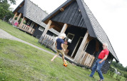 Kind und Erwachsener spielen Fußball vor schwarzen Holzhütten im Wood Lodge, Holiday park De Boshoek, Niederlande.