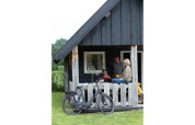 Gezin ontspant op de veranda van een Wood Lodge bij Holiday park De Boshoek, Nederland, met fiets ervoor.