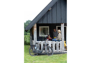 Famille se détend sur la terrasse d’un lodge en bois à Holiday park De Boshoek, Pays-Bas, avec un vélo devant.