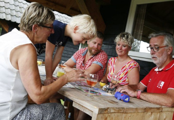 Familie nyder et brætspil sammen på terrassen ved Wood Lodge i ferieparken De Boshoek, Holland.