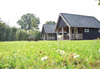 Zwei Holzhütten auf einer grünen Wiese im Ferienpark De Boshoek in den Niederlanden bei Sonnenschein.