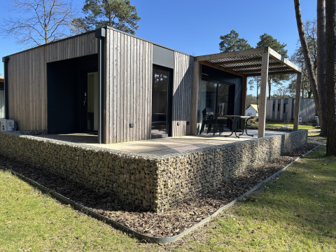 Domus 4+2 lodge met hedendaagse houten buitenzijde, ruim terras en buitenzitje in een groene omgeving.