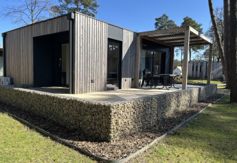 Domus 4+2 lodge met moderne houten gevel, groot terras en buitenzitje te midden van natuurlijke omgeving.