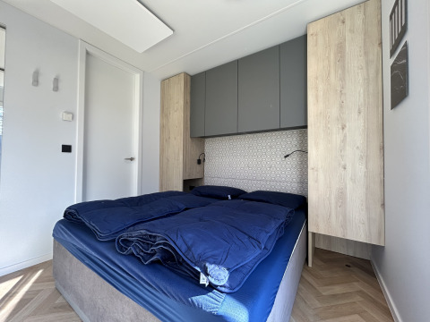 Slaapkamer met blauwe dekens en houten kasten in Domus 4+2 lodge op Zilverstrand, België.