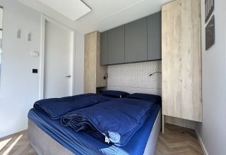 Slaapkamer met blauwe dekens en houten kasten in Domus 4+2 lodge op Zilverstrand, België.