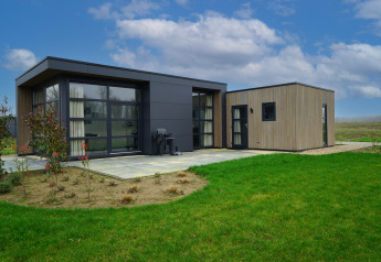 Moderne glampingindkvartering på landet med store vinduer, grøn græsplæne og blå himmel.