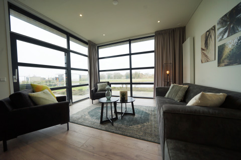 Moderne glamping woonkamer met grote ramen, comfortabele grijze banken en uitzicht op het landschap.