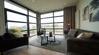 Salon glamping moderne avec grandes fenêtres, canapés gris confortables et vue sur la campagne verdoyante.