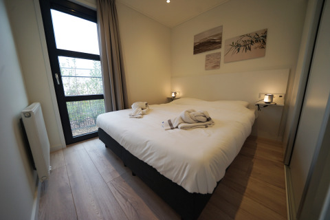 Moderne glamping-accommodatie met comfortabel tweepersoonsbed, groot raam, lichte muren en wanddecoratie.