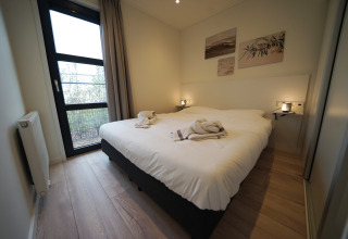 Moderne glamping-accommodatie met comfortabel tweepersoonsbed, groot raam, lichte muren en wanddecoratie.