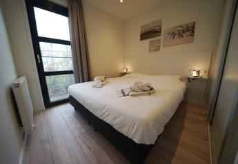 HĂ©bergement glamping moderne avec lit double confortable, grande fenĂȘtre, murs clairs et dĂ©cor mural Ă©lĂ©gant.