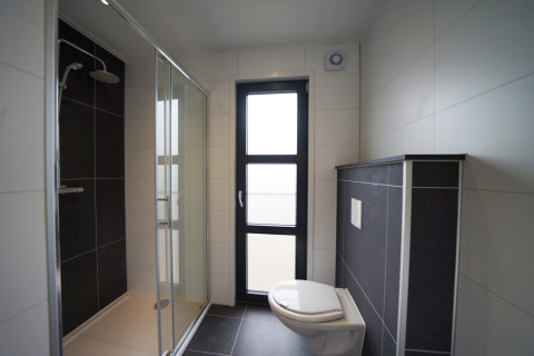 Moderne glampingbadkamer met douchecabine, wandtoilet en groot raam, stijlvol en licht ingericht.