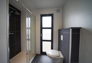 Moderne glampingbadkamer met douchecabine, wandtoilet en groot raam, stijlvol en licht ingericht.