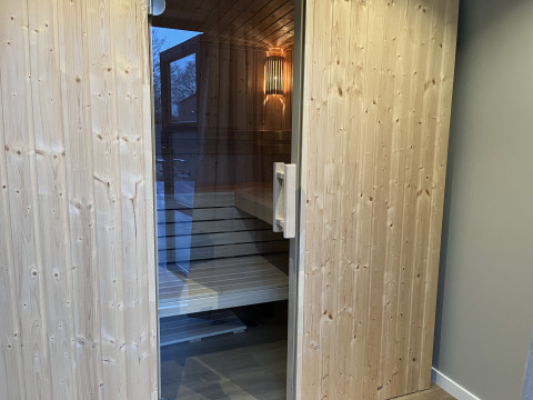 Moderne houten sauna met glazen deur bij een glamping accommodatie, perfect om te ontspannen.