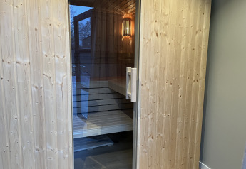 Sauna moderne en bois avec porte vitrée dans un hébergement glamping, propice à la détente.