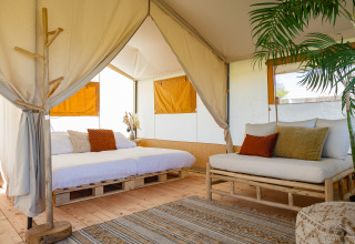 Vista interior de una tienda safari lodge con muebles de madera, cojines acogedores y plantas en Países Bajos.