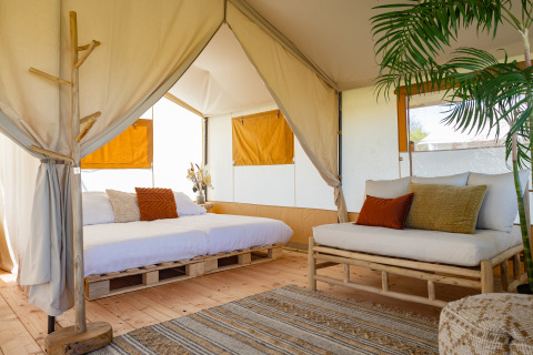 Binnenzicht op een safari tent lodge met houten meubels, gezellige kussens en planten in Nederland.