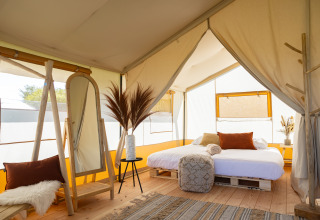 Interior de la tienda Safari Tent Lodge en TinyParks Cast Away, Países Bajos, con cama grande y decoración acogedora.