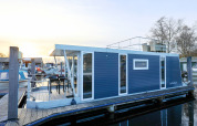 Hausboot im Hafen mit modernem Design, blauer Fassade, Terrasse und Dachterrasse, Niederlande, Sonnenuntergang.