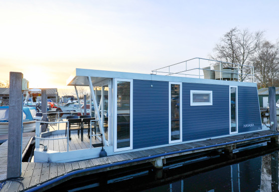 Casa flotante moderna llamada 'Havana' atracada en un puerto deportivo en Holanda, con terraza y azotea.