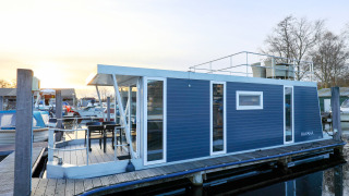 Hausboot im Hafen mit modernem Design, blauer Fassade, Terrasse und Dachterrasse, Niederlande, Sonnenuntergang.