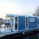 Casa flotante moderna llamada 'Havana' atracada en un puerto deportivo en Holanda, con terraza y azotea.