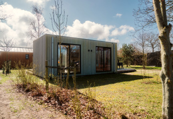 En moderne lodge kaldet Duunroos på Holiday park De Klepperstee i Holland, omgivet af grønne træer og buske.