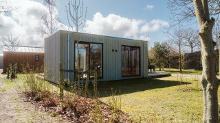 Moderne lodge Duunroos op vakantiepark De Klepperstee in Nederland, omgeven door natuur en bomen.