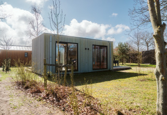 En moderne lodge kaldet Duunroos på Holiday park De Klepperstee i Holland, omgivet af grønne træer og buske.