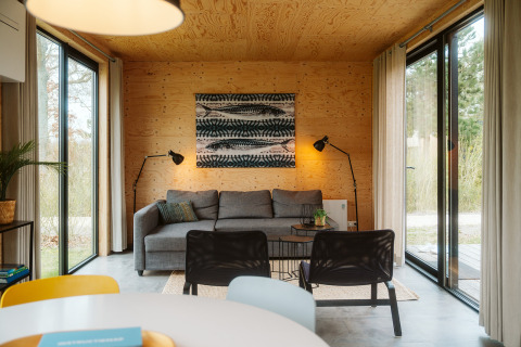 Cabaña moderna con paredes de madera, grandes ventanales y sofá gris en Duunroos, De Klepperstee.