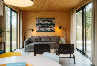 Cabaña moderna con paredes de madera, grandes ventanales y sofá gris en Duunroos, De Klepperstee.