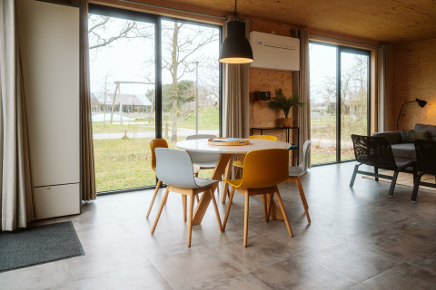 Modern dining area with colorful chairs, large windows, and lounge at Duunroos lodge, De Klepperstee, Netherlands.