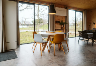 Moderne eethoek met gekleurde stoelen en grote ramen in de Duunroos-lodge, De Klepperstee, Nederland.