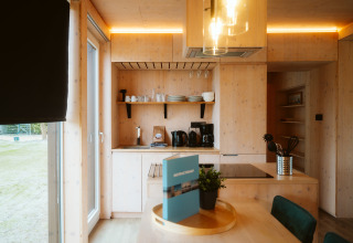 Moderne køkkeninteriør i lyst træ med spisebord, vindue og hyggelig belysning i Ark Shelter, Holland.