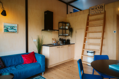 Interior acogedor de The Hoagte tiny house con cocina, sofá azul y escalera en De Klepperstee, Países Bajos.