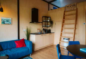 Knus interieur van The Hoagte tiny house met keuken, blauwe bank en houten trap bij De Klepperstee, Nederland.