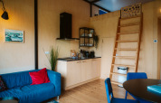 Cozy interior of The Hoagte tiny house featuring a kitchenette, blue sofa, and wooden ladder at De Klepperstee.