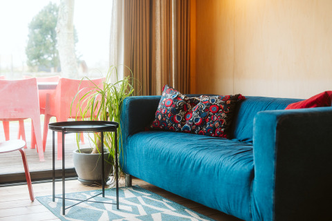 Salon du tiny house The Hoagte au Holiday Park De Klepperstee avec canapé bleu et coussin coloré.