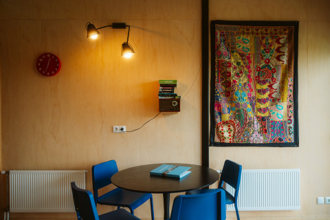 Interno della tiny house The Hoagte al parco De Klepperstee, con tavolo rotondo e arazzo colorato alle pareti.