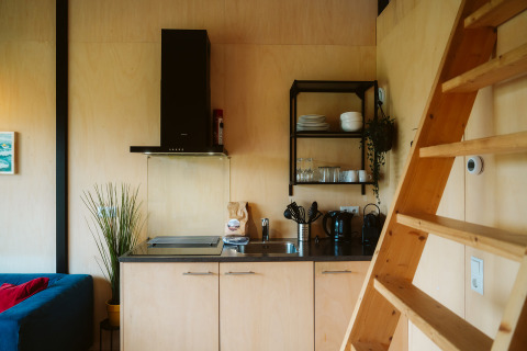 Moderne kitchenette met houten interieur en ladder in een tiny house op vakantiepark De Klepperstee, Nederland.