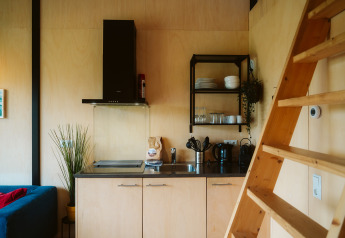 Moderne kitchenette met houten interieur en ladder in een tiny house op vakantiepark De Klepperstee, Nederland.