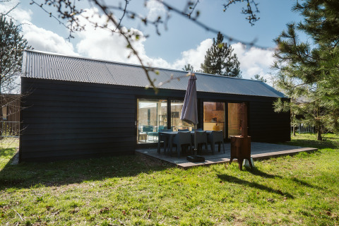 Moderne lodge van donker hout met terras en tuinmeubilair bij De Klepperstee, Nederland.
