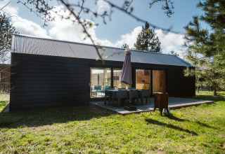 Moderne lodge van donker hout met terras en tuinmeubilair bij De Klepperstee, Nederland.