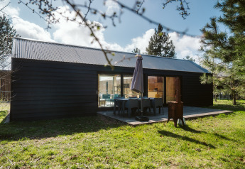 Moderne lodge van donker hout met terras en tuinmeubilair bij De Klepperstee, Nederland.