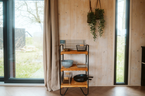 Coin douillet à Punt, tiny house à De Klepperstee, Pays-Bas, avec étagère, plantes et grandes fenêtres.