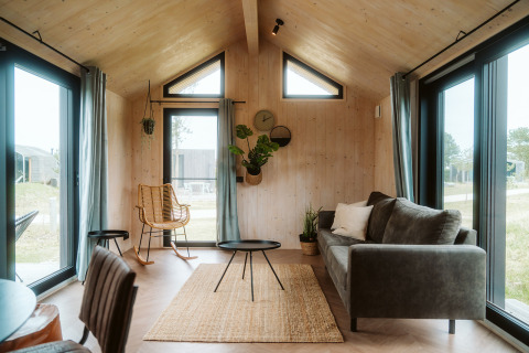 Zona de estar luminosa y moderna en la tiny house Melle del Holiday park De Klepperstee, Países Bajos, con grandes ventanales.