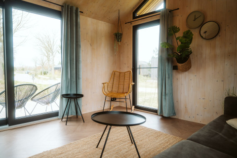 Salon lumineux avec grandes fenêtres, meubles modernes et plantes vertes dans une tiny house à Melle, Pays-Bas.