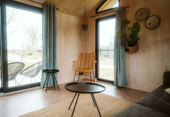 Soggiorno luminoso con ampie finestre, arredi moderni e piante verdi in una tiny house a Melle, Paesi Bassi.