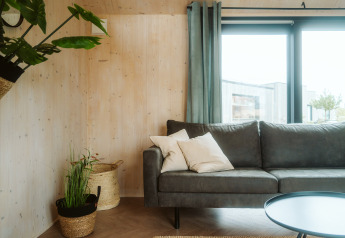 Lichte en gezellige woonkamer in Melle, een tiny house op vakantiepark De Klepperstee, met zetel, planten en grote ramen.