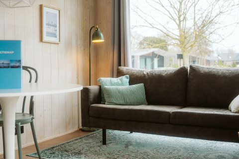 Moderne stue i Tiny Rebel, Holiday park De Klepperstee, med grøn sofa, læselampe og stort vindue.